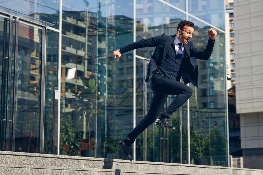 Businessman jumping into action from the top of a set of stairs leading up to office building.