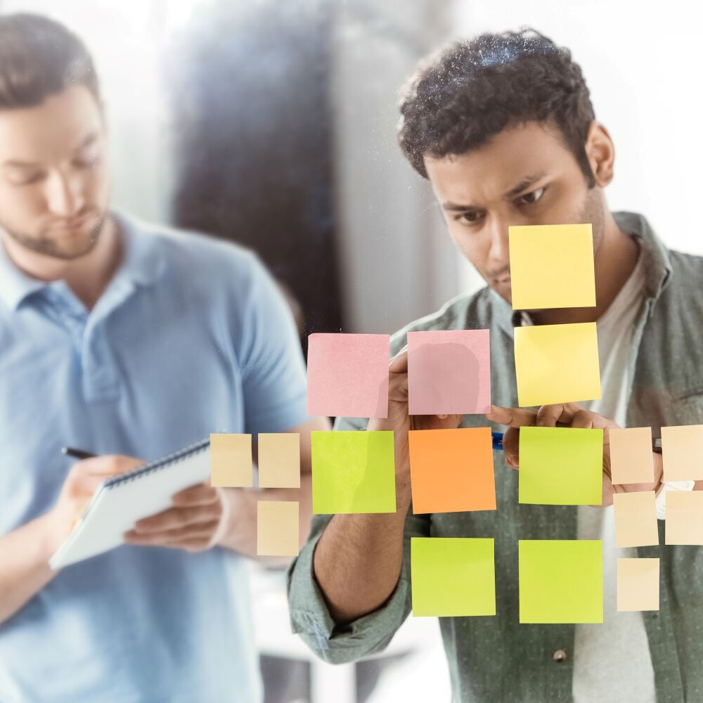 Two casual businessmen review colorful post it notes to turn consumer insights into concepts for marketing.