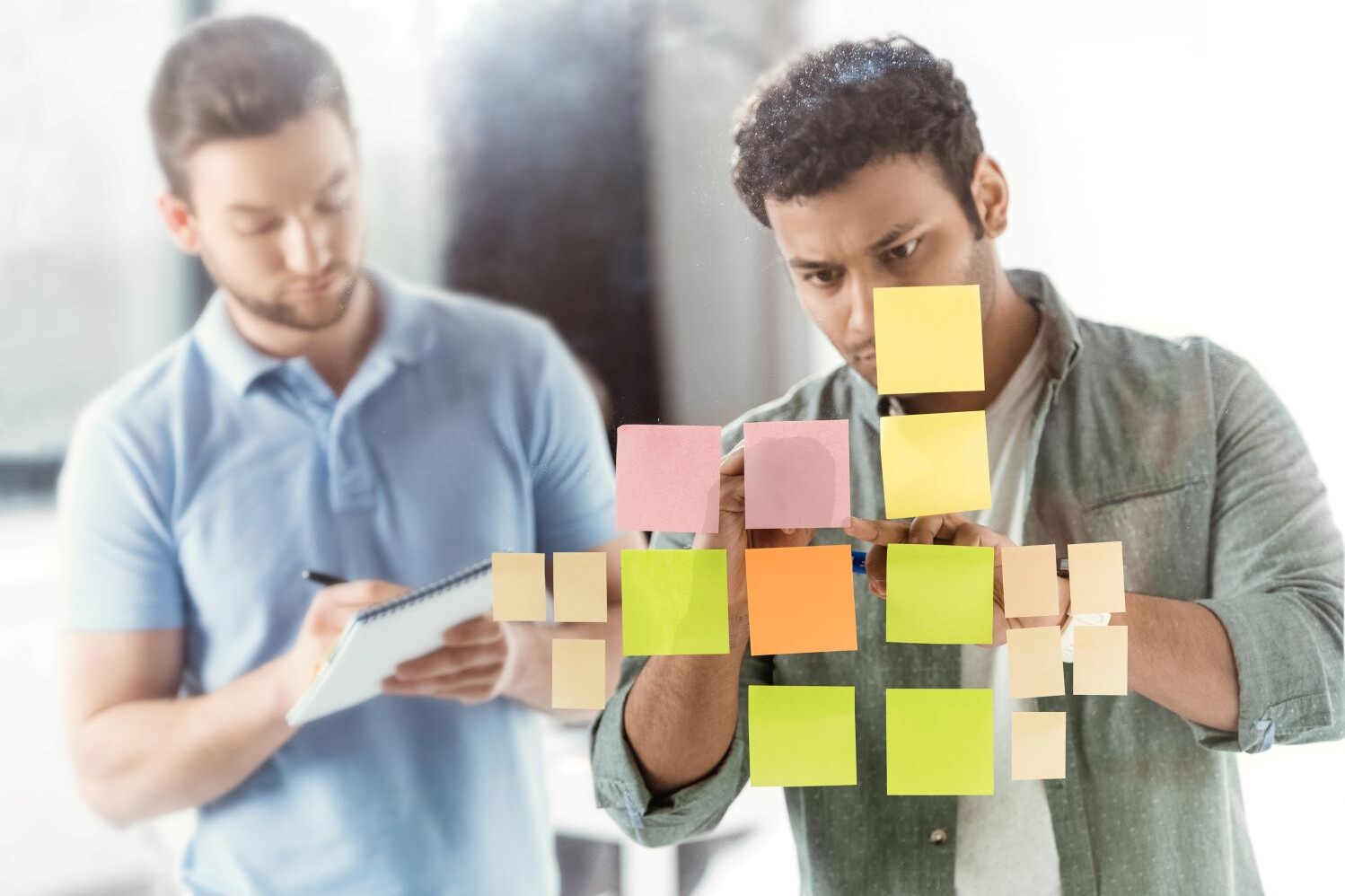 Two casual businessmen review colorful post it notes to turn consumer insights into concepts for marketing.