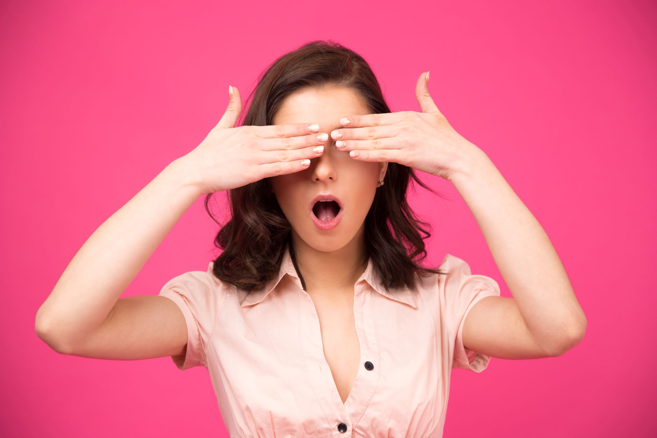 Woman covering her eyes with hands against pink background