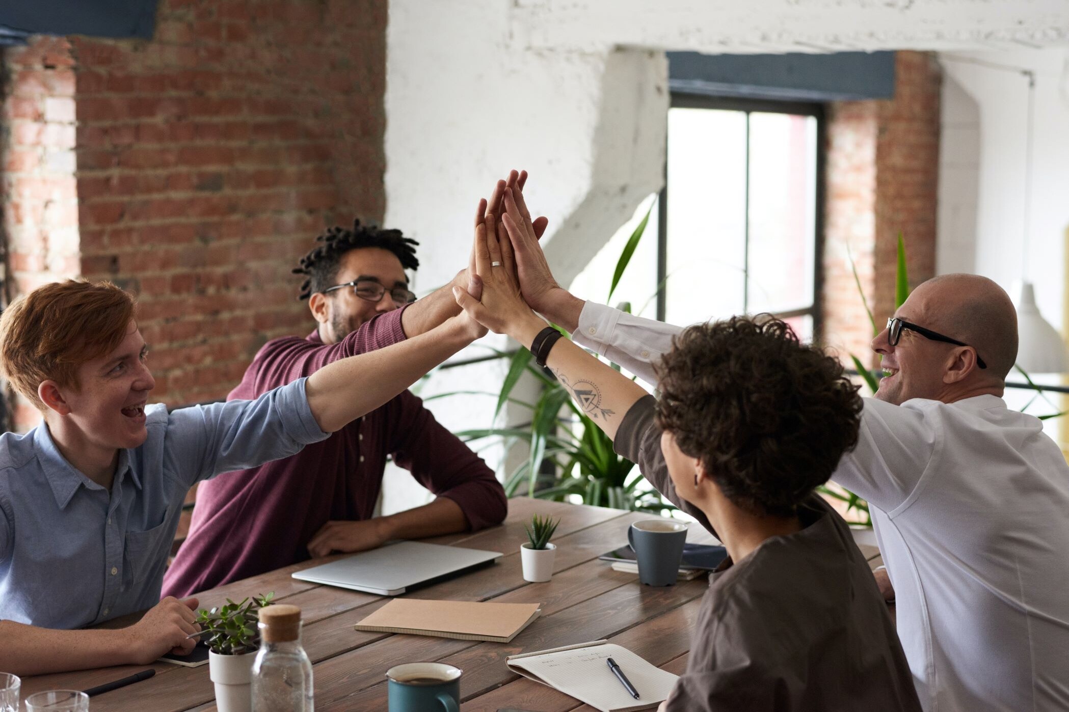 Group of four coworkers high five while sitting together at a table