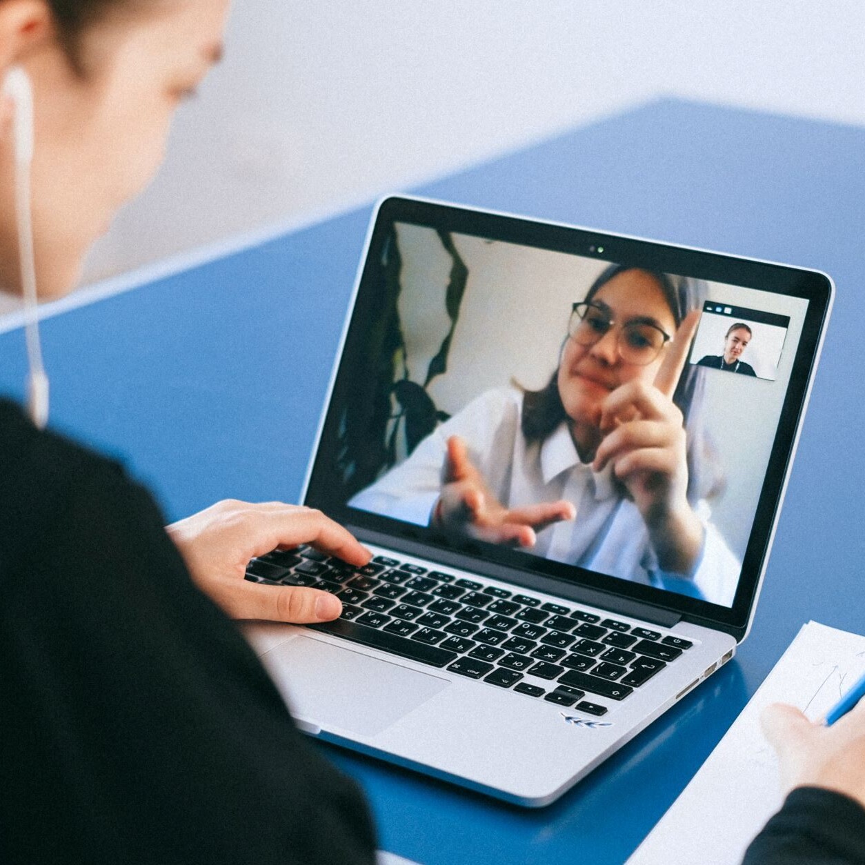 A woman sitting out of focus having a conversation with another woman via video chat on her laptop.