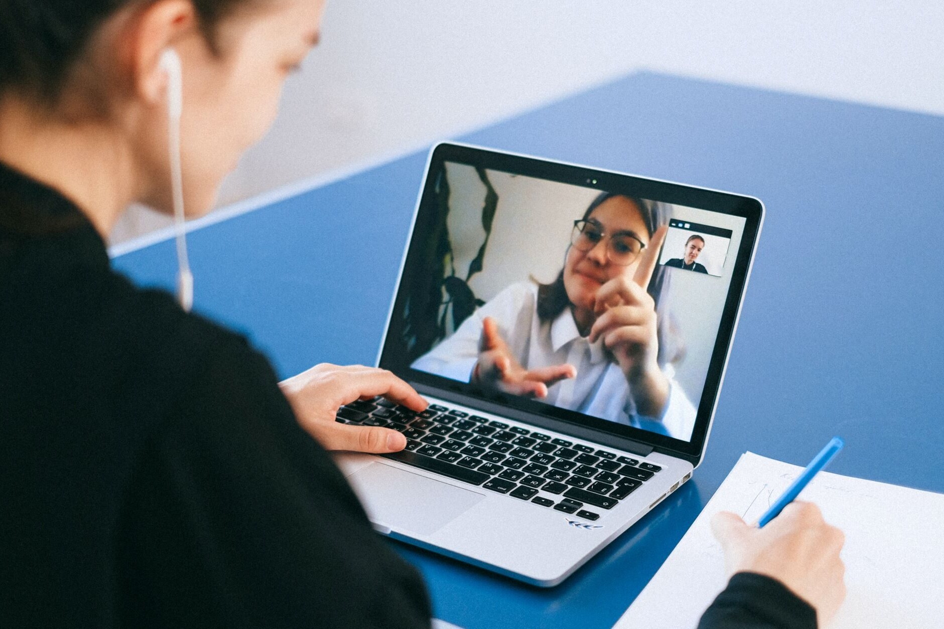 A woman sitting out of focus having a conversation with another woman via video chat on her laptop.